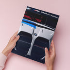 A person holds a printed poster featuring a close-up of a silver and black BMW Motorsport car front, against a soft pink background.