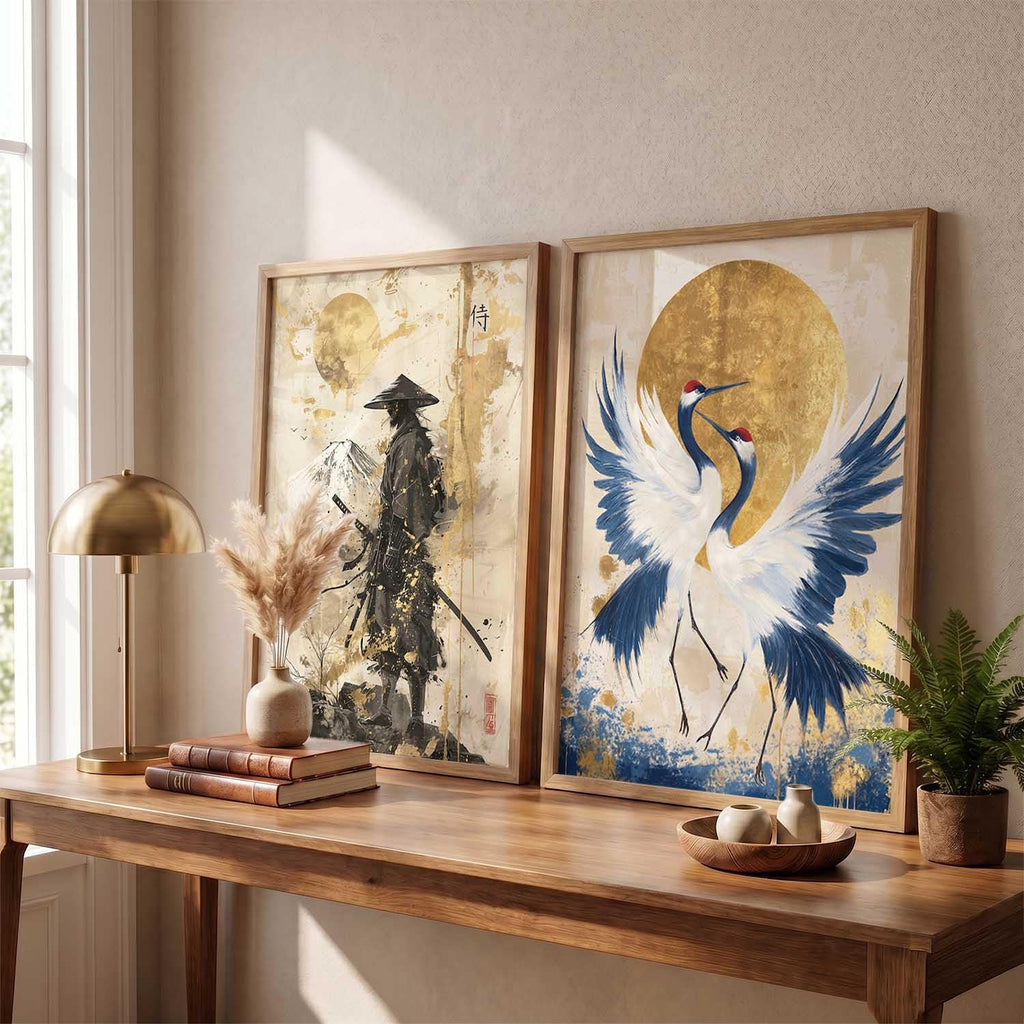 Two framed Japanese-style art prints displayed side-by-side on a beige wall above a wooden console table. The left print depicts a samurai warrior in black and gold, and the right print shows a white crane with blue details against a large gold sun.