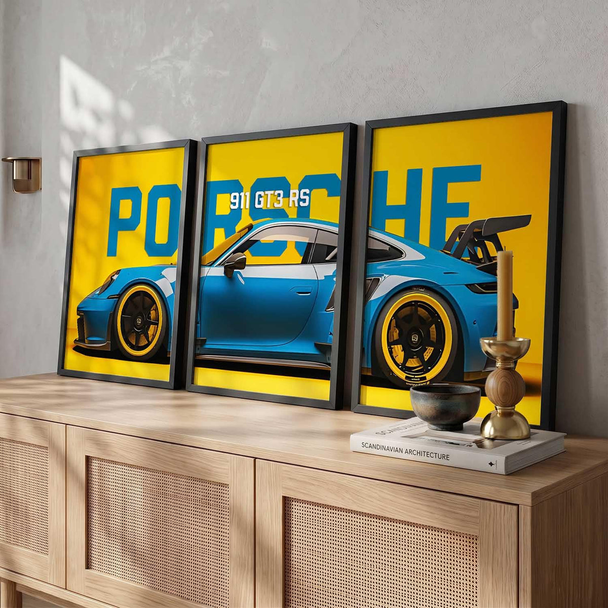 A three-panel framed wall art set featuring a blue Porsche 911 GT3 RS on a bright yellow background, displayed above a light wood cabinet in a styled interior.