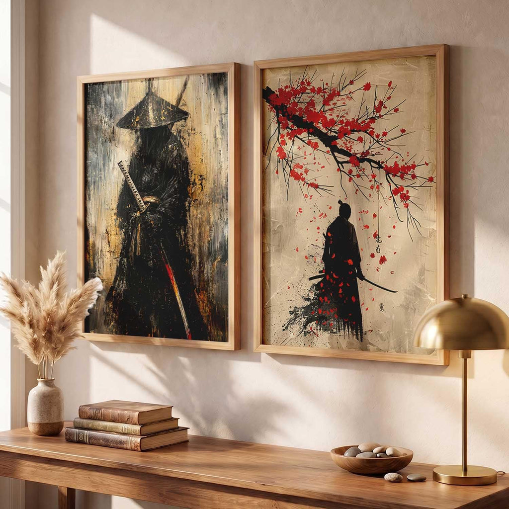 Two framed abstract art prints with Japanese-inspired warrior motifs hang on a beige wall above a wooden console table. The left print shows a dark hooded figure with a sword, and the right print shows a black silhouette under red blossoms.