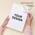 A person holds a white 300GSM gumming sheet with the text 'YOUR DESIGN' printed on it, peeling back the top-right corner to show the sticky backing. The background is a solid light beige, with text overlays reading '300GSM GUMMING SHEET' and 'PEEL & STICK ON WALL'.