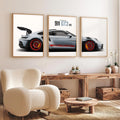 A three-panel framed wall art set showing a silver Porsche 911 GT3 RS, displayed in a modern living room setting above a wooden console table and a cream-colored armchair.